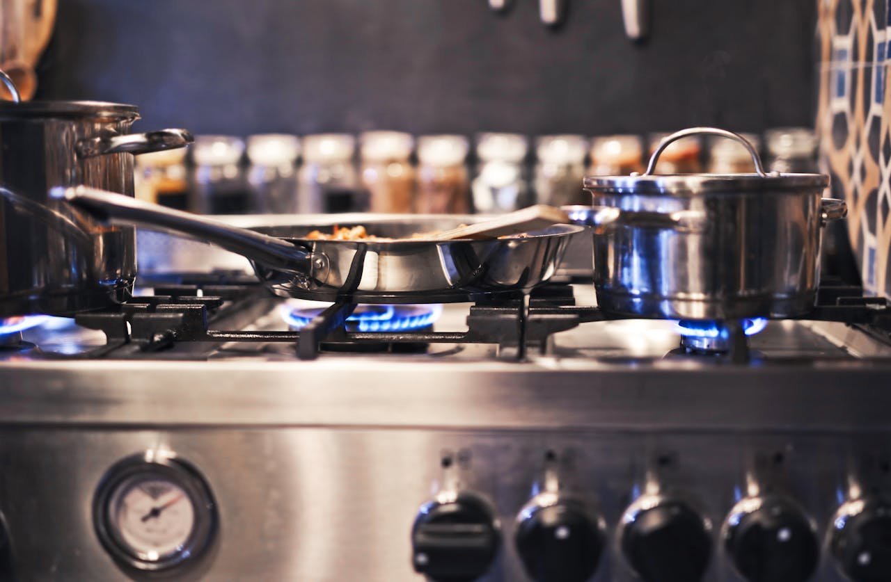 Cooking utensils including pots and pans on a gas stove with blue flames.